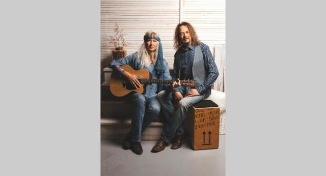 Ein Mann und eine Frau sitzen auf einer Bank, die Frau hat eine Gitarre in der Hand