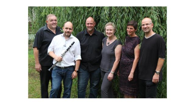 Die Band steht im Freien vor dichtem Grün