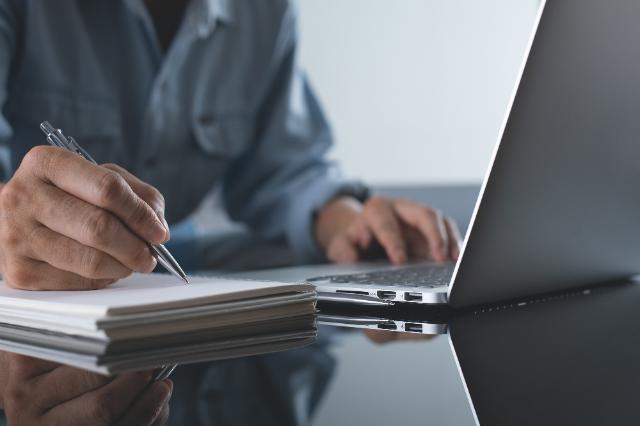 Eine Person sitzt am Laptop und schreibt etwas auf