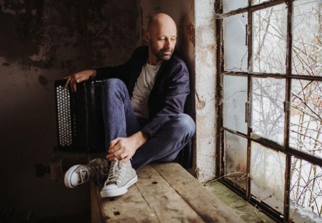 Ein Mann mit Akkordeon sitzt an einem Fenster.