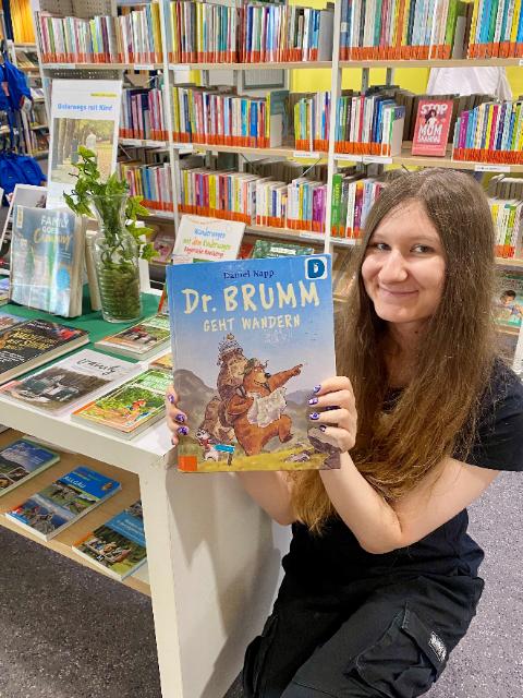Eine Frau sitzt mit einem Buch in der Hand vor einem Büchertisch