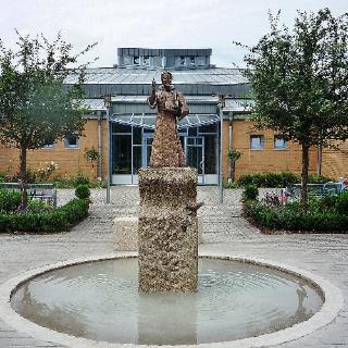 Ansicht auf das Gemeindezentrum St. Benedikt, davor steht ein Brunnen mit Skulptur