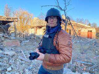 Fotograf Till Mayer steht mit Kamera vor Kriegsgebiet