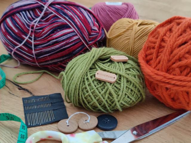 Bunt verstreut liegen Wollknäuel, Knöpfe, Scheren, Nadeln. 