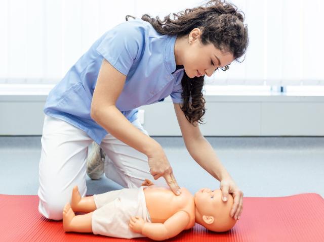 Kinderkrankenpflegerin zeigt Herzdruckmassage an Puppe