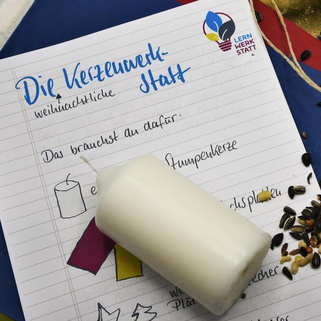 Eine weiße Stumpenkerze liegt quer über einem Blatt Papier, auf dem "Kerzenwerkstatt" steht.