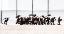 Etwa 30 Ensemblemitglieder des Nürnberger Akkordeonorchesters vor einem Gebäude fotografiert.  Einige haben aufgespannte Regenschirme in der Hand, andere tragen ein Akkordeon, andere einen Koffer. Ein Mann in Frack, etwas abseits der Gruppe, posiert von einem Tretroller aus und winkt der Gruppe zu - es ist der Leiter des Orchesters. Die Personen sehen vergnügt aus.