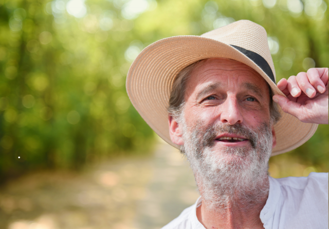 Ein Mann mit einen Sonnenhut auf dem Kopf, den er mit einer Hand am Rand festhält