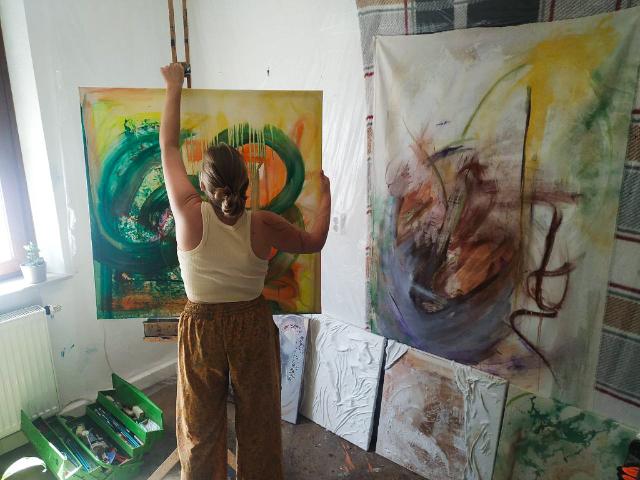 Person steht mit dem Rücken zur Kamera vor bunt bemalten Leinwänden.