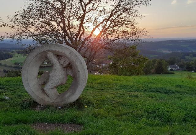 Radförmige Steinskultur auf grüner Wiese. Im Hintergrund weiter Blick ins Tal. Sonnenuntergang.