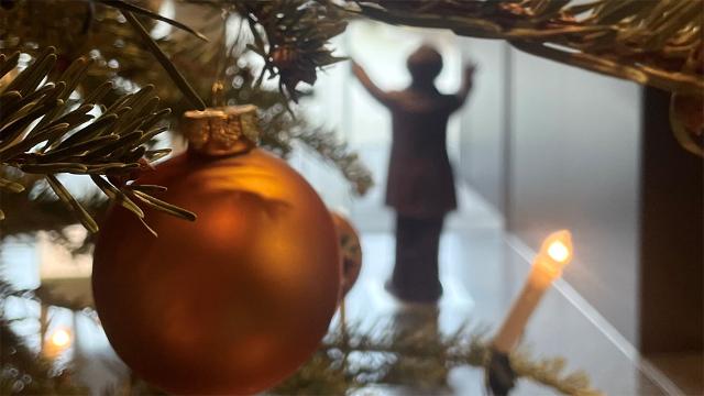 Im Hintergrund sieht man eine dirigierende wagner-Figur. Im Vordergrund eine Christbaumkugel, beleuchtet von einer Kerze am Weihnachtsbaum