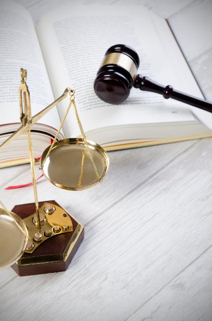 Auf dem Bild ist ein Buch, ein Richterhammer und die Waage der Gerechtigkeit zu sehen.