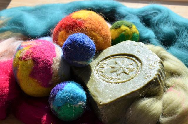 Bunte Wolle und Bälle aus Wolle liegen wild durcheinander. Darauf liegt ein grünes geprägtes Stück Seife. 