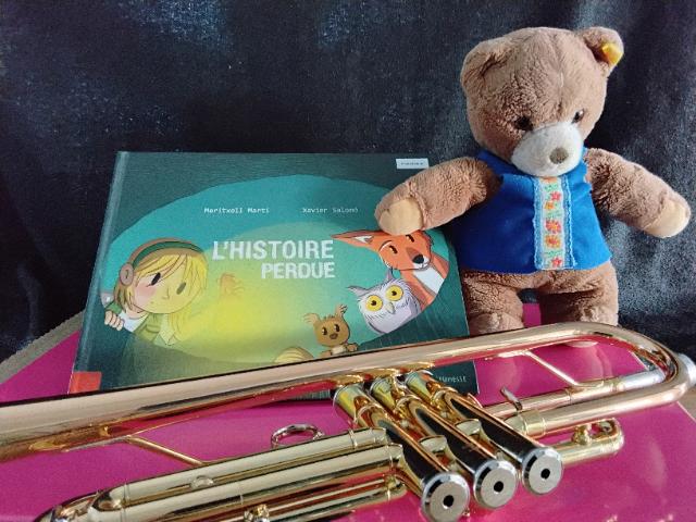 Das Kinderbuch Die verlorene Geschichte zusammen mit einem Stoffteddybär und einem Instrument.