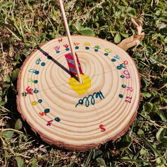 Auf einer runden Holzscheibe sind Zahlen aufgemalt und ein Stab steckt darin. 
