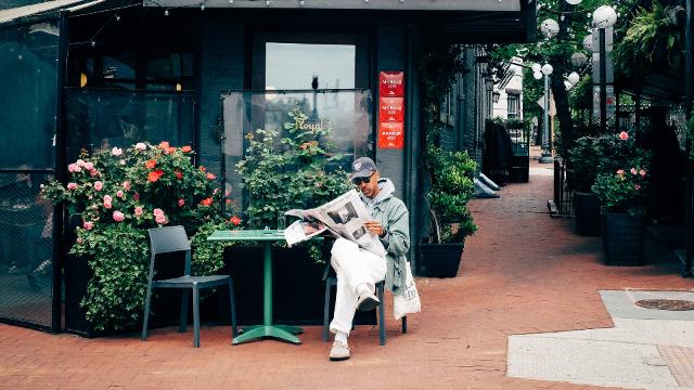 Oddisee sitzt vor einem Haus und liest Zeitung