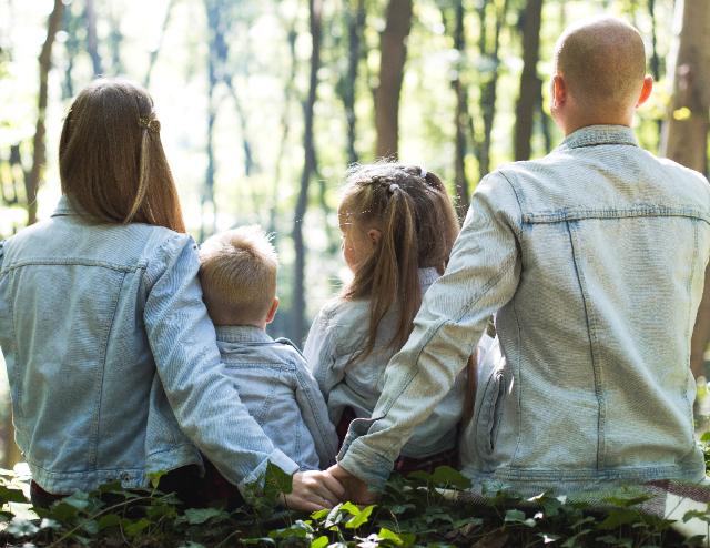 Foto einer Familie von hinten, sitzend im Wald mit Mutter, kleinem Sohn, kleiner Tochter und Vater. 