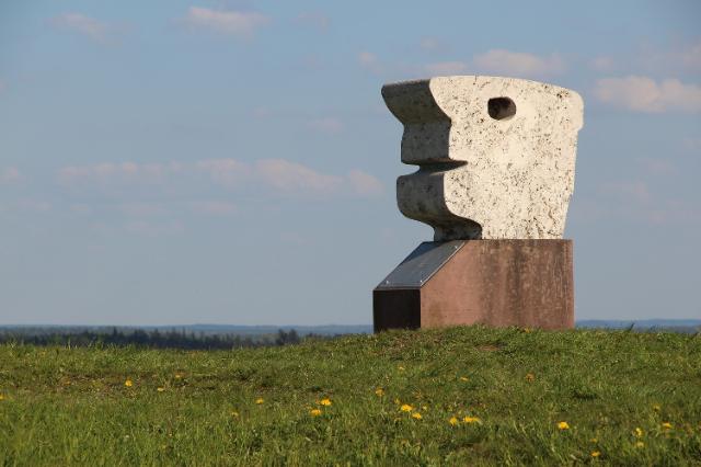 Abstrakte Steinskultur auf grüner Wiese vor blauem Himmel