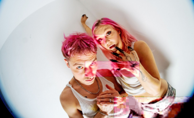 Zwei Personen vor einer weißen Wand mit pinken Haaren