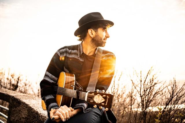 Felix Yunger mit seiner Gitarre in der Natur sitzend