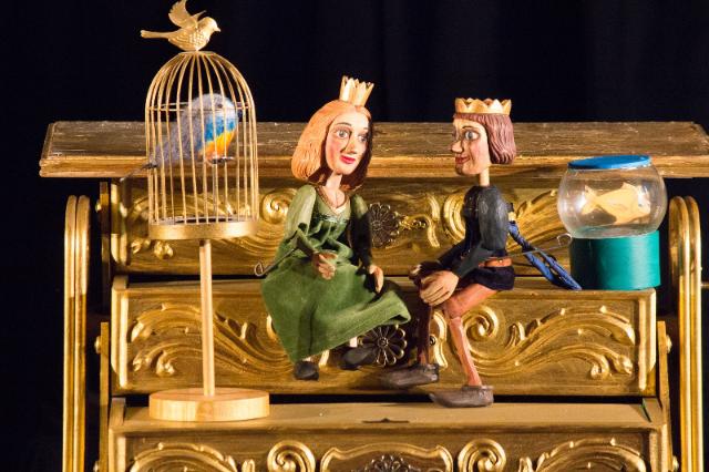 Ein goldener Schrank, zwei Holzpuppen mit Kronen, ein kleiner Vogelkäfig mit hölzernen Vogel.