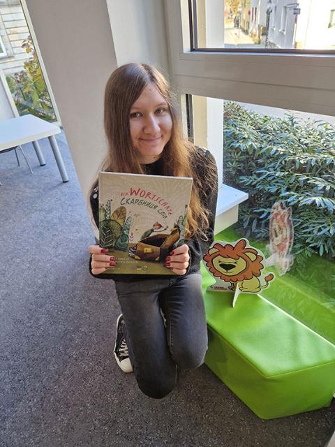 Frau sitzt mit Buch in der Hand auf grüner Bank.