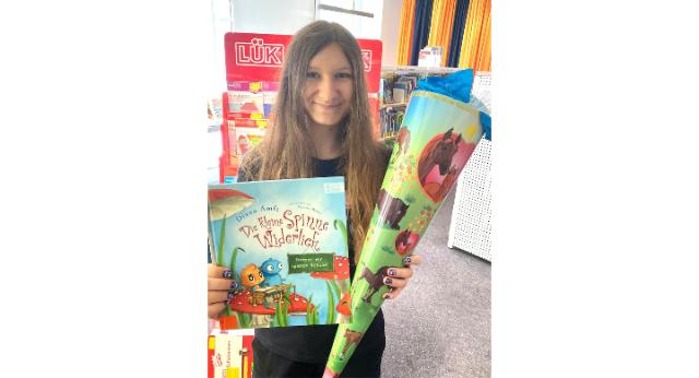 Eine junge Bibliotheksmitarbeiterin hält ein Bilderbuch und eine Schultüte in der Hand.