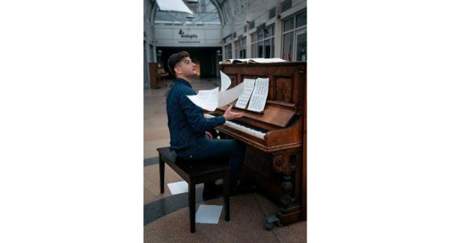 Denisov sitzt am Klavier und wirft Notenblätter in die Luft