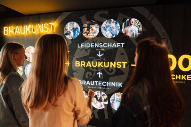3 Personen vor einer Ausstellungswand